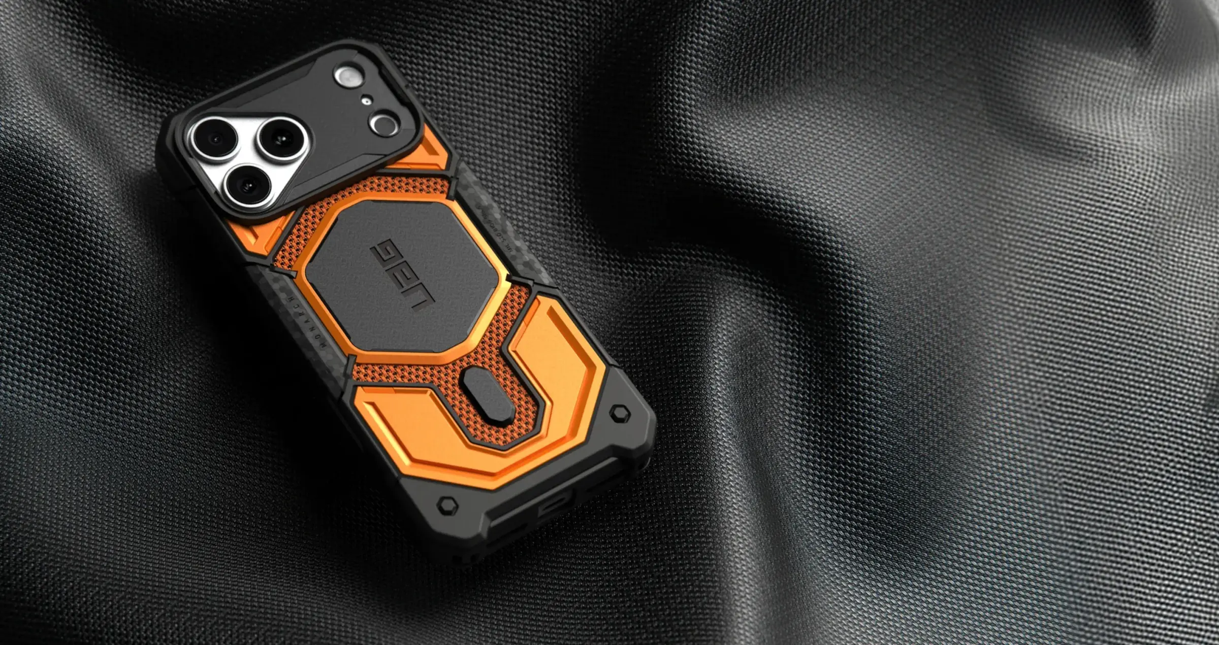 橘黑配色 UAG Monarch Pro 保護殼斜放在深灰織布上