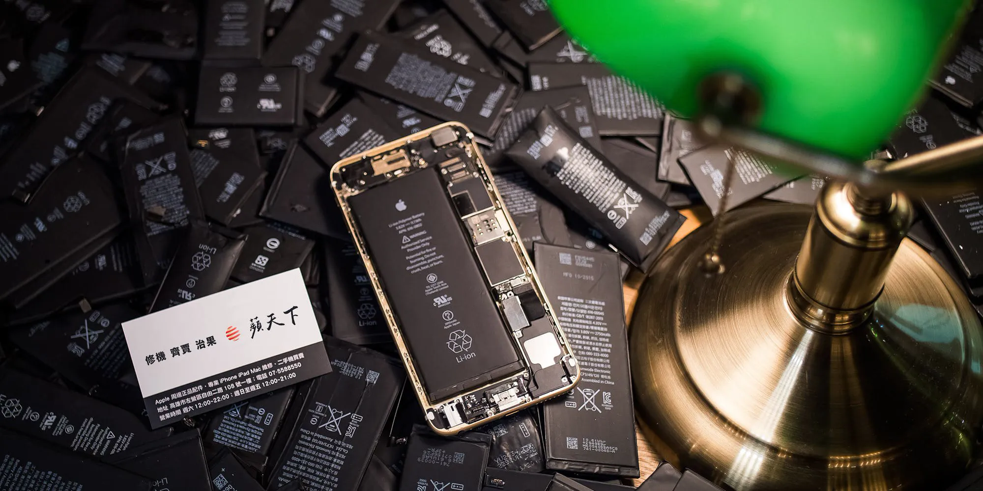 散落的 iPhone 原廠電池與拆開的 iPhone,旁邊是蘋天下名片
